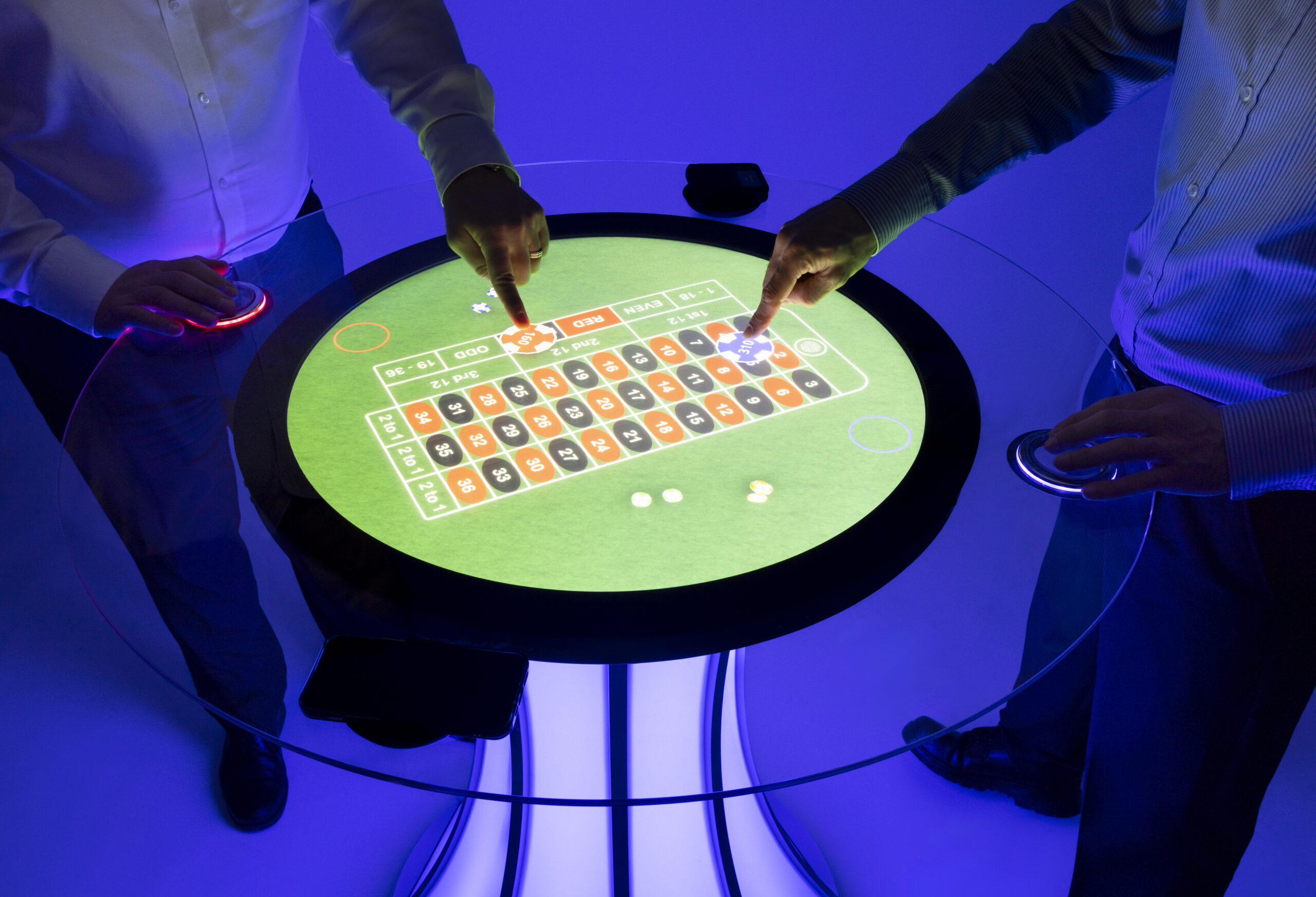 Two people playing roulette on a round touchscreen table